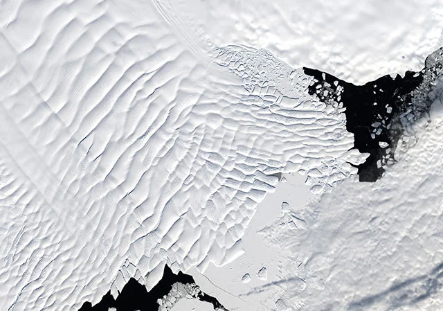 An overhead photo of Totten Glacier oozing off the Antarctic coast and floating on the ocean.