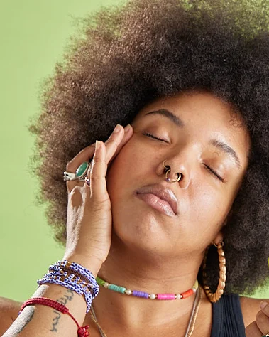 A Black person with an afro rubs a cream into her cheek blissfully