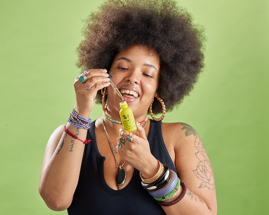 A Black person gleefully decants a dropper of green oil from a green bottle