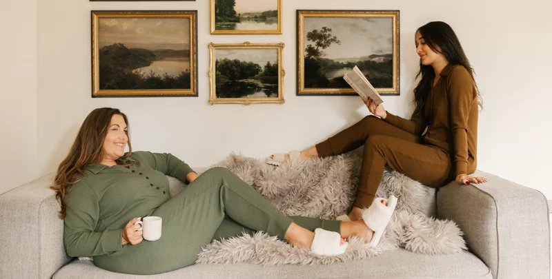 2 women sat on couch wearing green and brown rompers