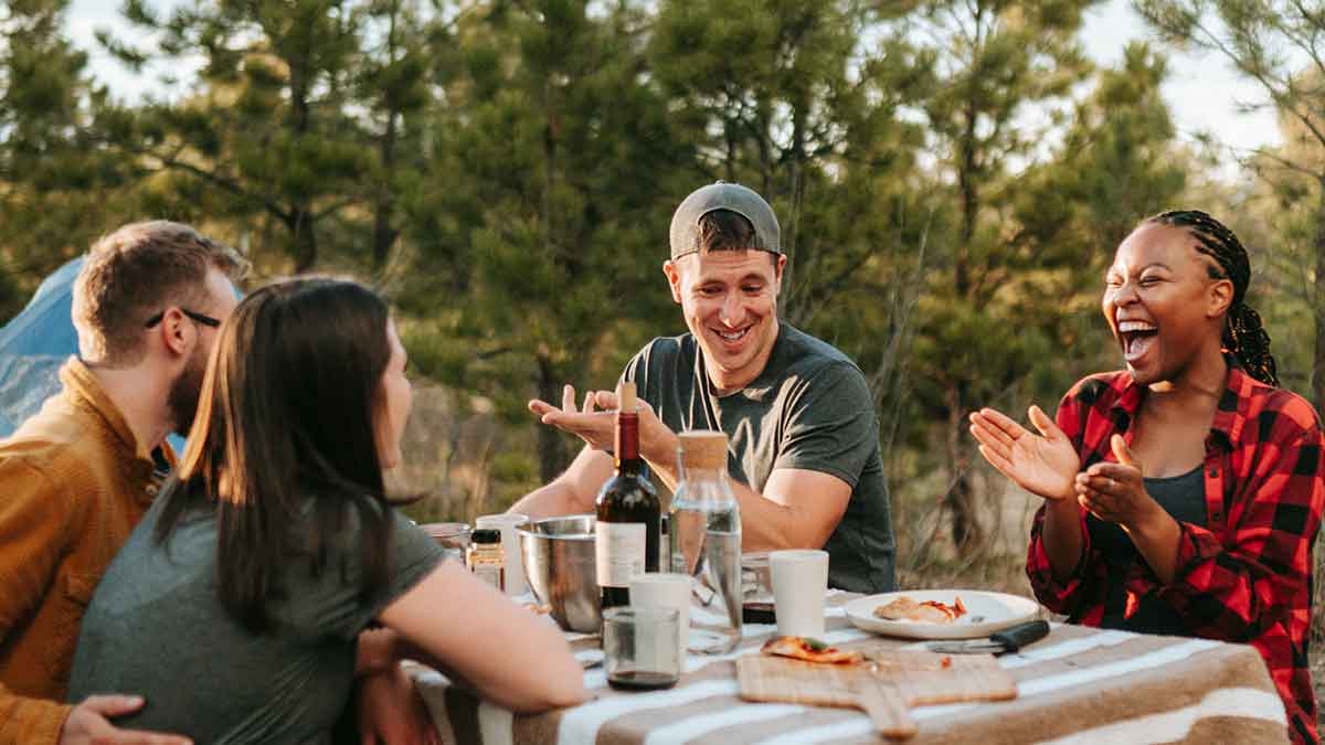 A group of friends laughing around a table, eating pizza and drinking wine