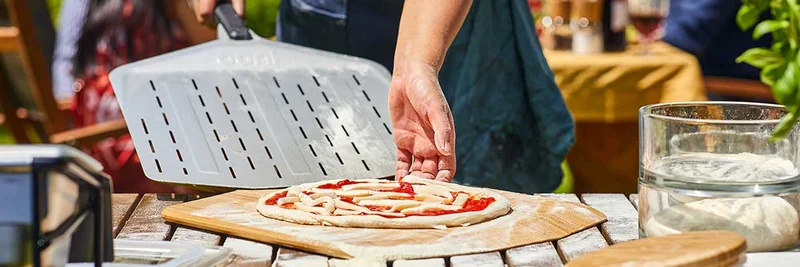 A raw pizza being slid onto a perforated pizza peel - learn tips like this with Ooni