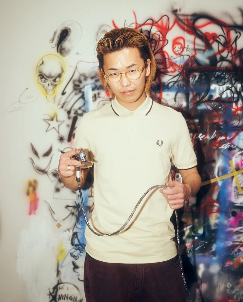 Asian male model standing on front of graffiti art wearing an ecru Fred Perry Polo Shirt
