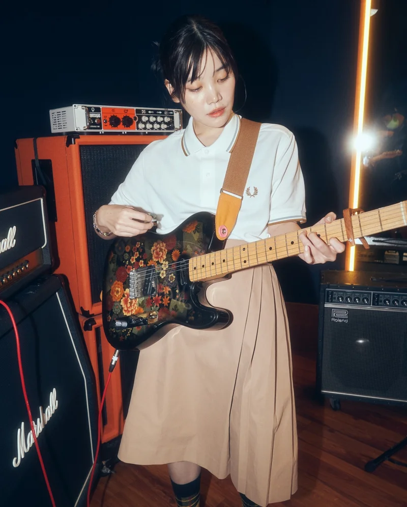 Asian female model wearing a white fred perry polo shirt playing electrice guitar in a music studio