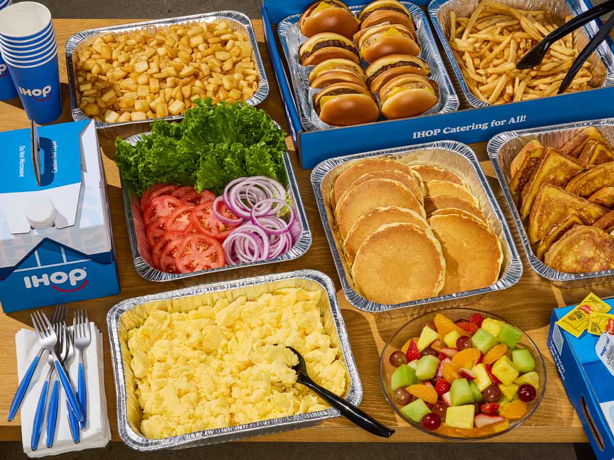 An assortment of IHOP Catering tins and packaging, including pancakes, scrambled eggs, and burgers, neatly laid out on a table.