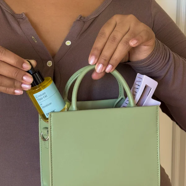 Person placing Prose Custom Hair Oil into green bag with purple claw clip Person placing Prose Custom Hair Oil into green bag with purple claw clip