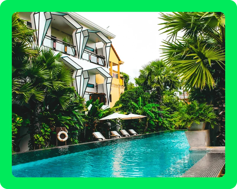 Image Description: Long, rectangular pool surrounded by tropical plants with 3D geometric architecture lining the outside of the hotel building.
