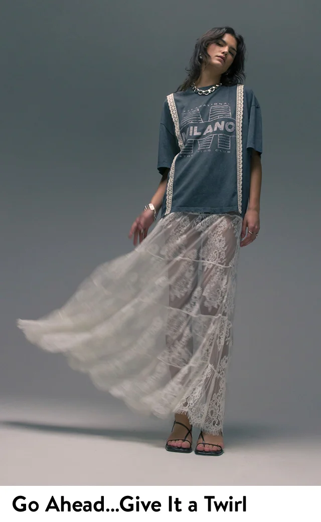 A woman wearing a sheer lace maxi skirt with a graphic tee and strappy flat sandals.