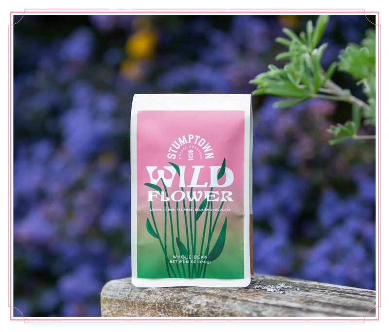 Bag of Stumptown Wild Flower coffee standing on a wooden surface with soft purple flowers blurred in the background. Headline reads: “So Good It’s Wild.”