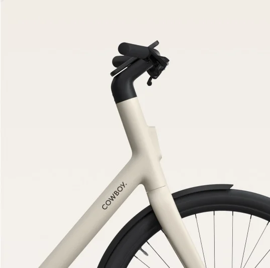 A render. a Cowboy e-bike frame, showing a minimalist design with a black saddle and sand-coloured frame.