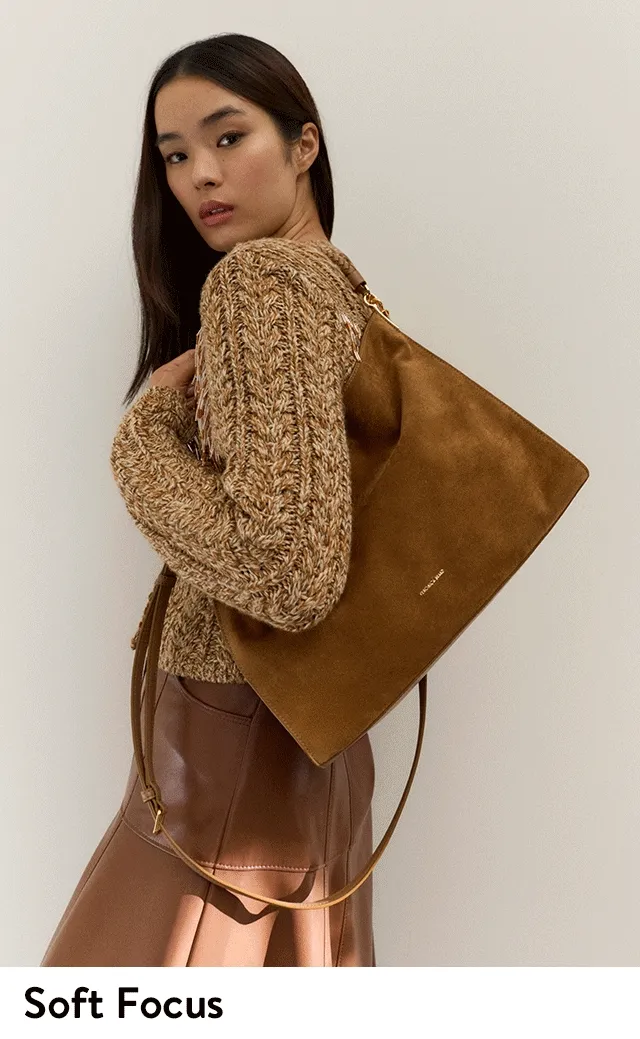 A woman in fall clothing carrying a brown suede bag.