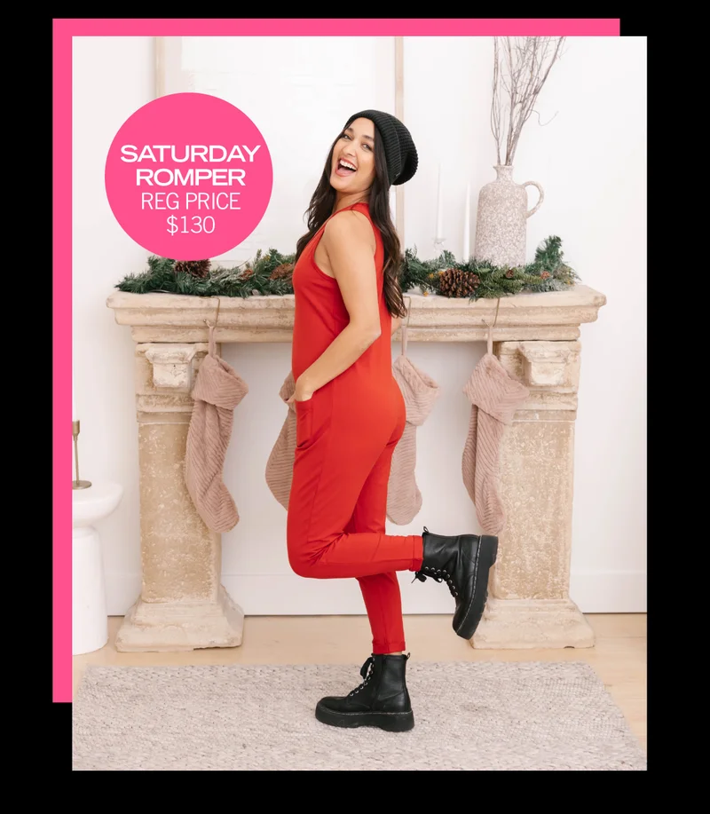 brunette wearing red romper and black hat stood in front of festive fireplace