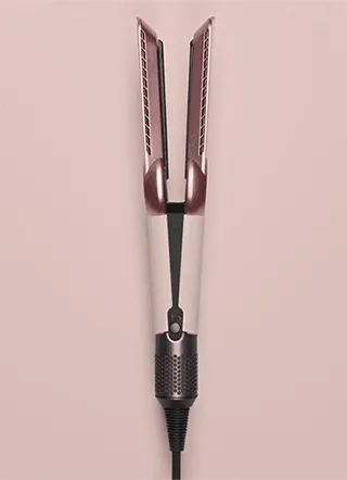 The Dyson Airstrait straightener in Ceramic pink and rose gold being revealed by silk