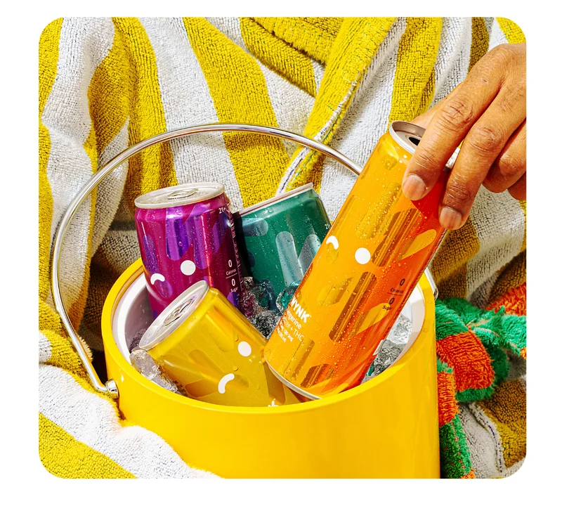 a photo of someone in a striped robe holding a cooler with 4 cans of wynk in all flavors.