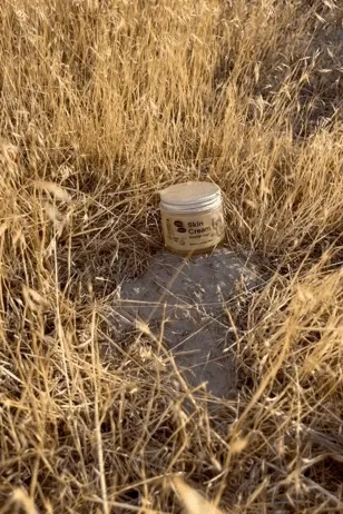 A tan jar of cream is shown in tall dried out grass