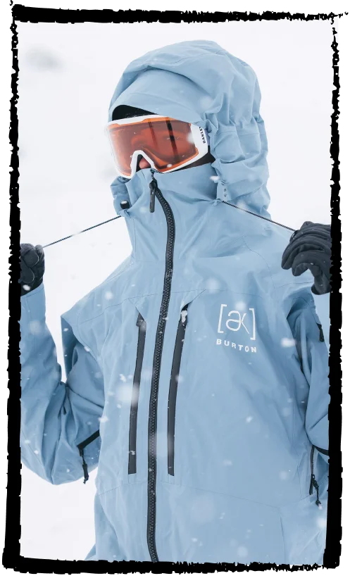Snowboarder wearing the Burton [ak]® Swash jacket in dusty blue in the mountains
