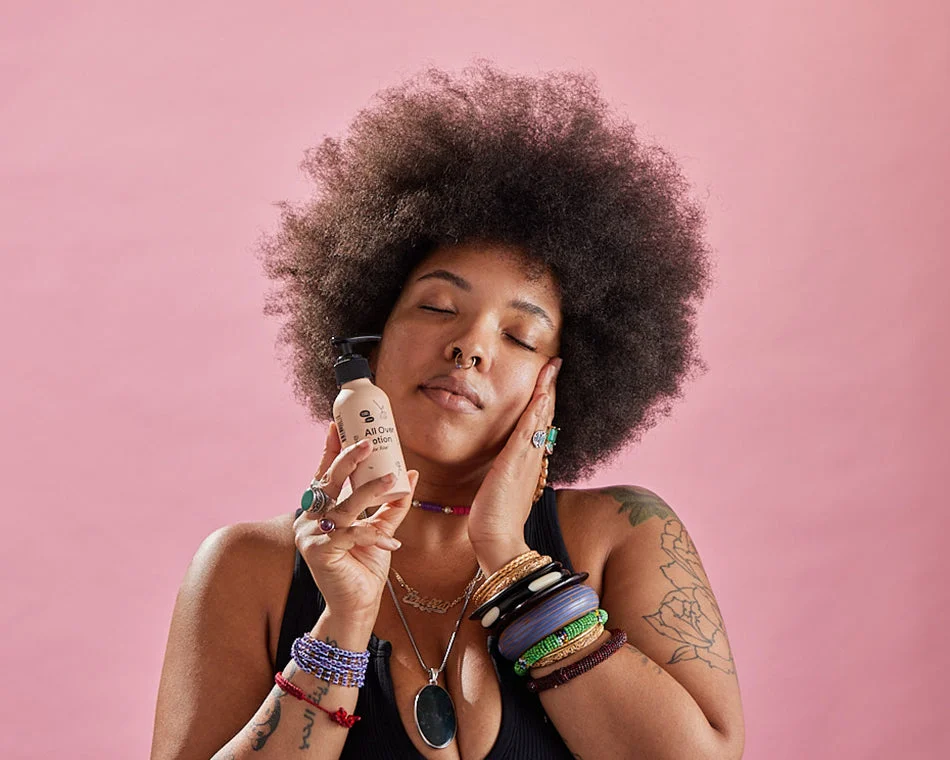 A Black person with an Afro rubs lotion on her cheek peacefully