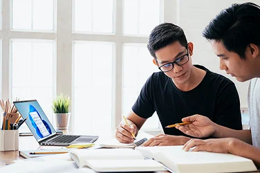 Two students studying using text books and a Dell laptop computer running Windows 11.