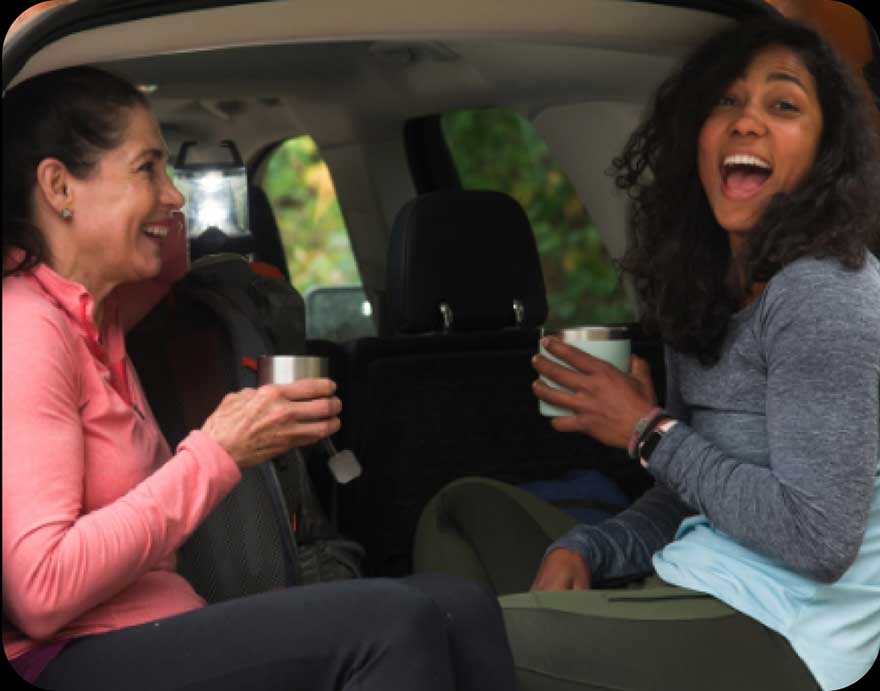 Two women sitting in the trunk of a parked Ford.