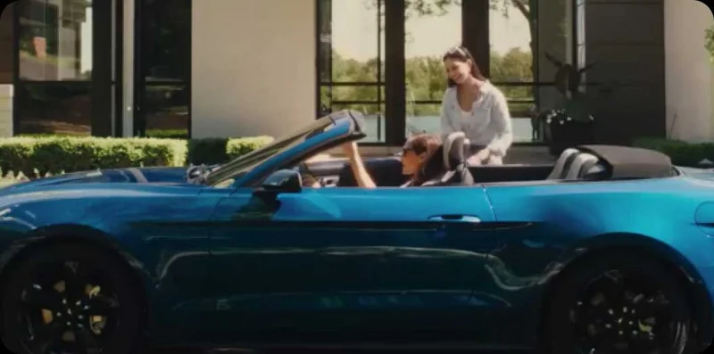 A woman sitting in a convertible talking to another woman.