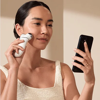 Woman holding smart phone and using TRINITY+ along with NuFACE Smart App