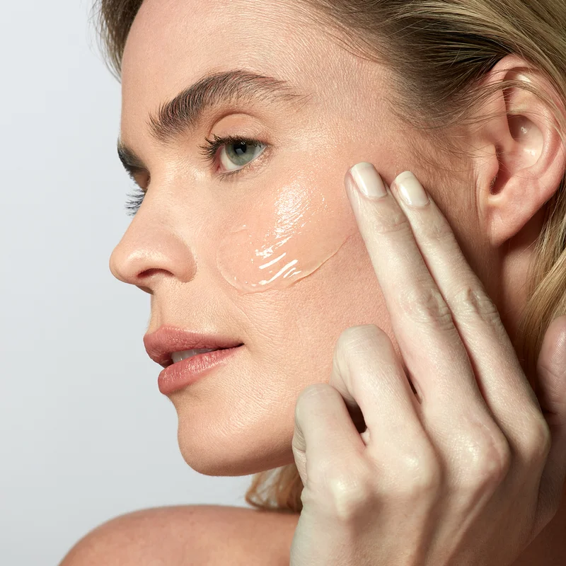 Woman applying activator gel onto face before beginning device treatment.