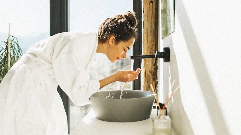 Image description: Woman washing face in bathroom sink