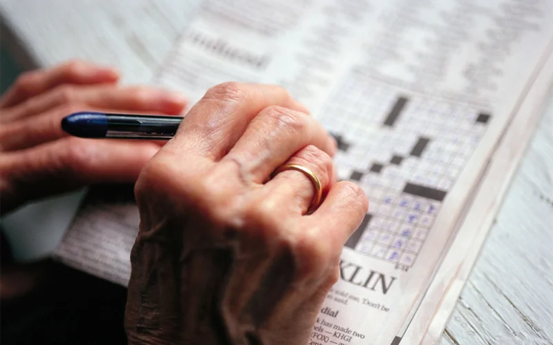 An elderly person works on a crossword puzzle.