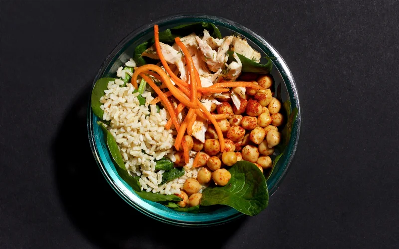 A bowl containing various sources of protein, including chicken, chickpeas, spinach, and whole grain rice.