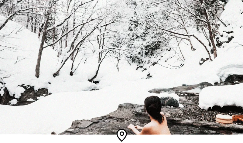 Image Description: A female traveler relaxing in an outdoor onsen in the middle of a snow-covered forest in Japan