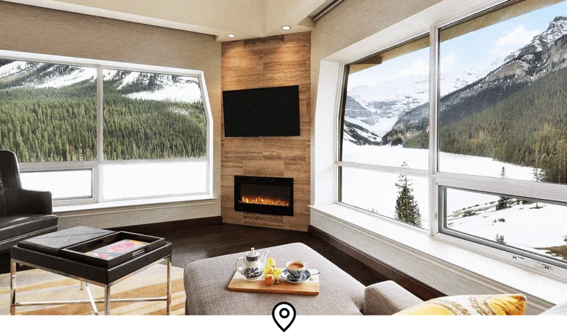 Image Description: Interior of a room in a luxe ski lodge, decked with a fireplace and sweeping views of pine forests and snow-capped peaks in Banff National Park