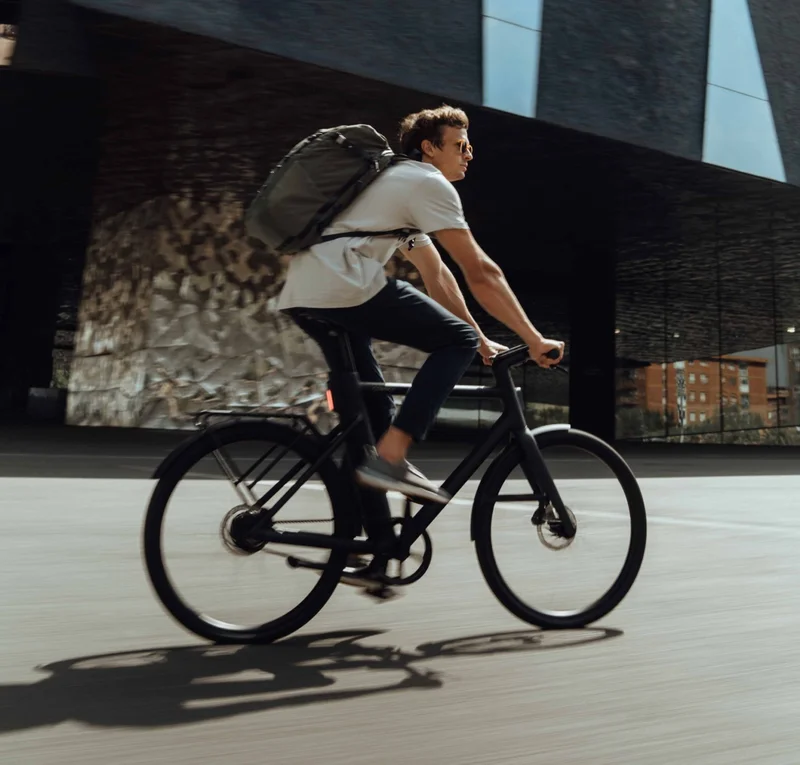 A photograph. A man rides a Cowboy bike in an urban setting.