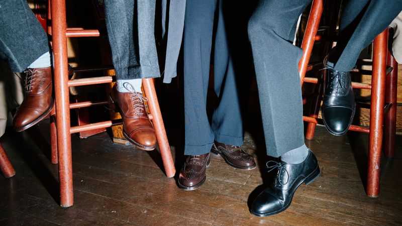 Three GQ staffers wearing men's Oxford shoes while sitting on barstools.