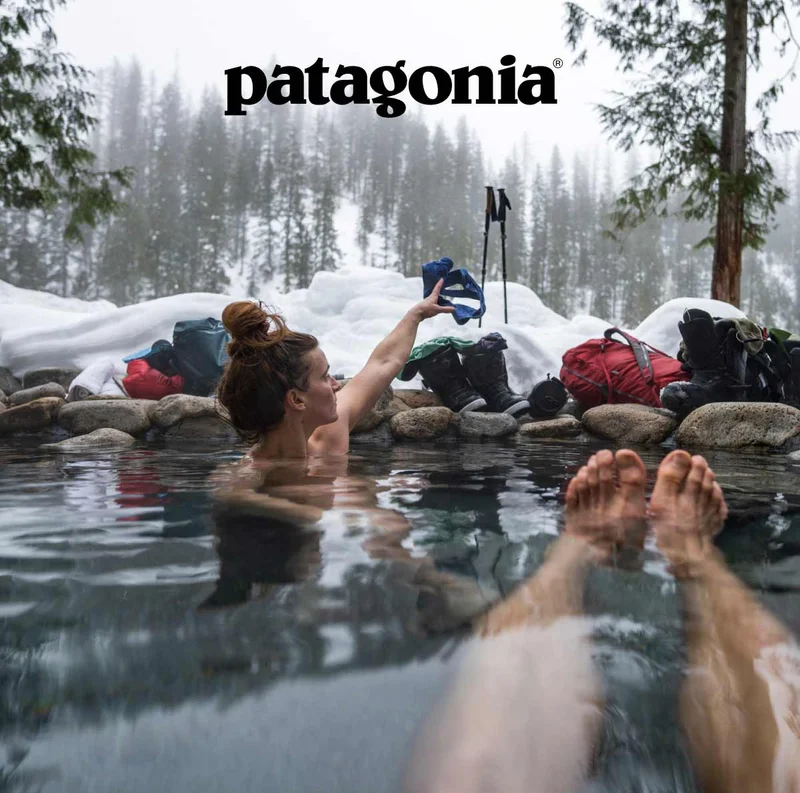 Two people sitting in a natural hot spring in a snow-covered forest.