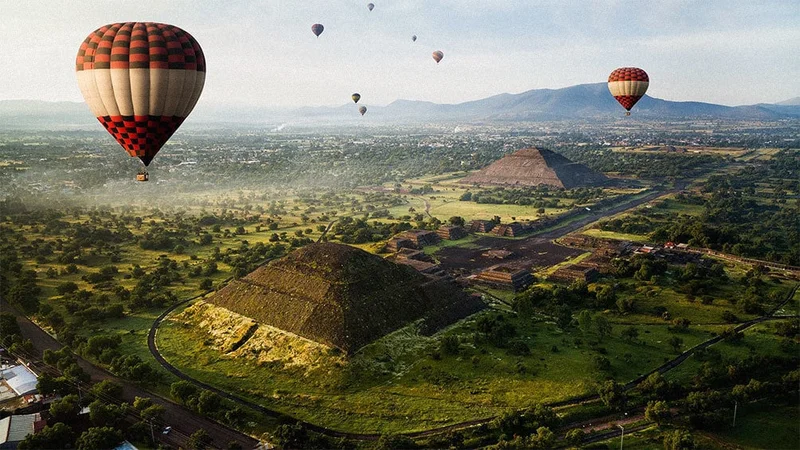 Image description: Hot air balloons flying in the sky at Teotihuacan, Mexico