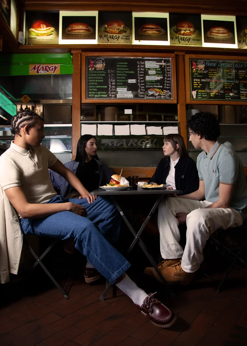 A group of 4 men and women enjoying food in an italian cafe wearing fred perry polo shirts