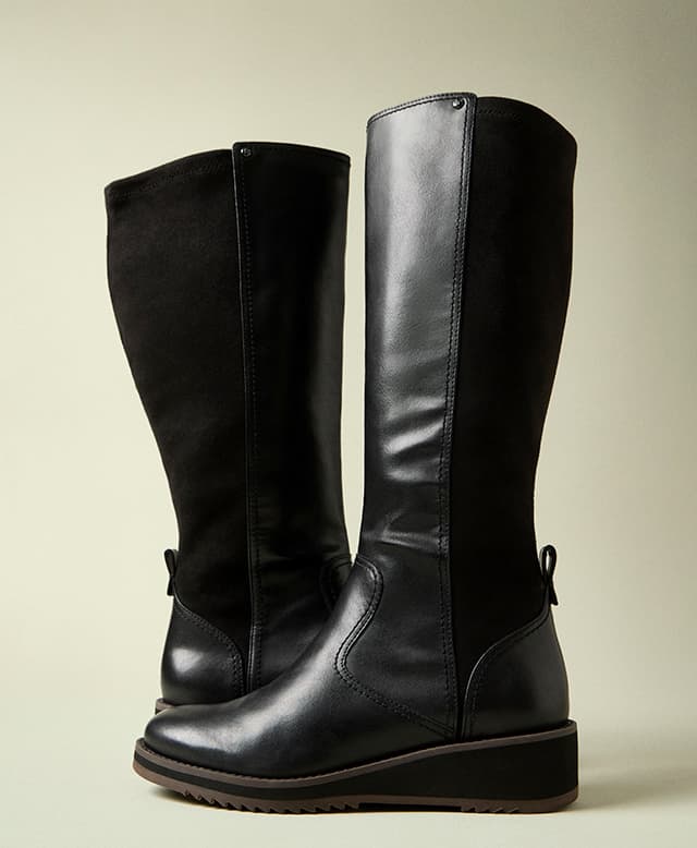 A pair of the Hush Puppies Madi Boots in black leather showcasing a comfortable stretch panel at back. Available in medium and wide width, wide calf. Shop Now