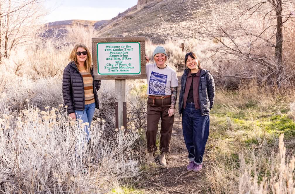 Three people stand by a sign at the Tom Cooke trailhead.