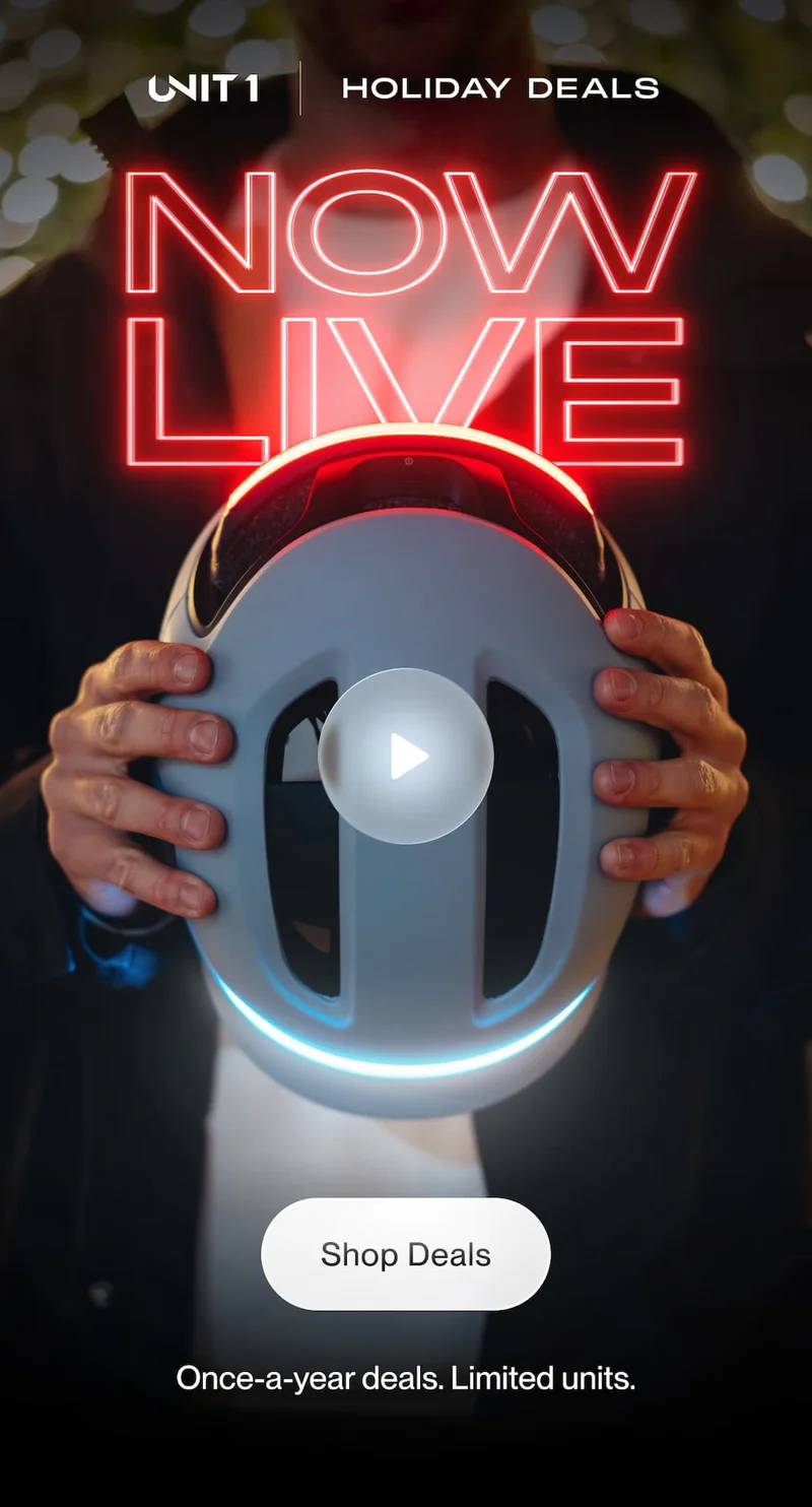 Hands holding a UNIT 1 smart helmet glowing with LED lights under the headline ‘NOW LIVE – Holiday Deals.’ Button below reads ‘Shop Deals.’ Once-a-year offers, limited units available.