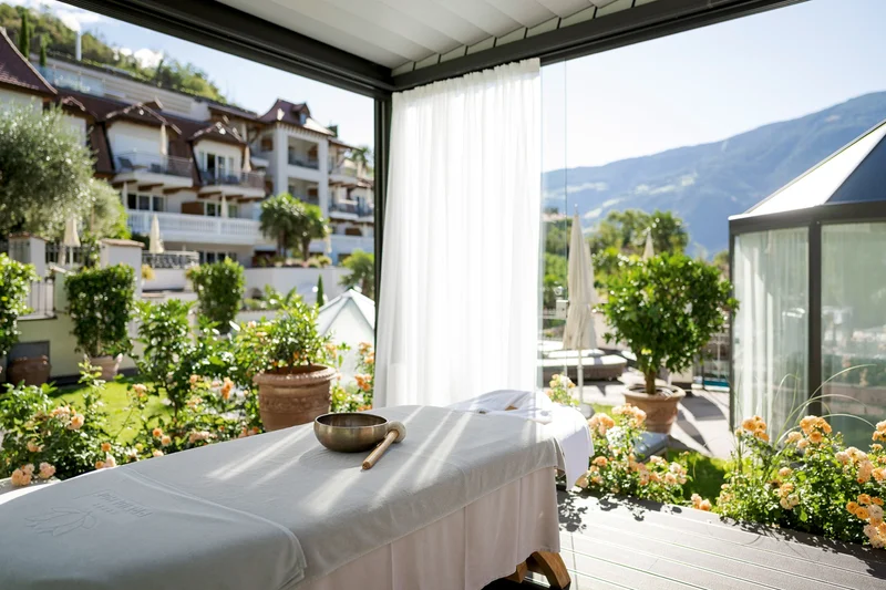 The corner of a panoramic room with views on greenery and hills, a massage bed just in front.