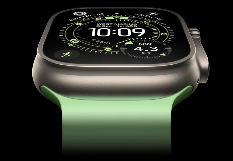 A close-up of a Natural Titanium Apple Watch Ultra 3 on a black background. The display shows the time and other dynamic info.