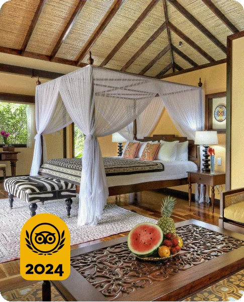 Image Description: A rustic room with an airy canopy over a bed. A table with fruit is in the foreground. A gold 2024 Travelers’ Choice Award Best of the Best badge is on the bottom left corner.