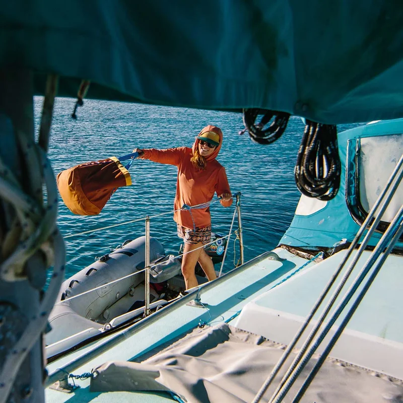 A person in a dinghy throws a bag onto a sailboat.