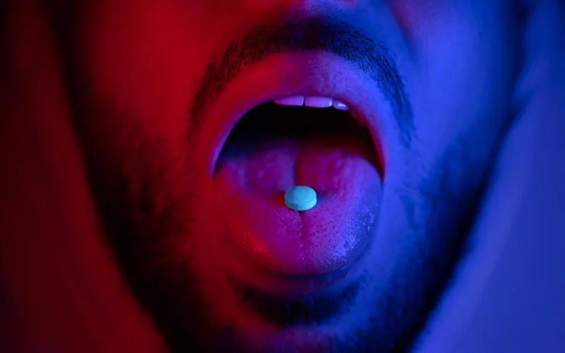 A pill rests on the tongue of a man’s open mouth