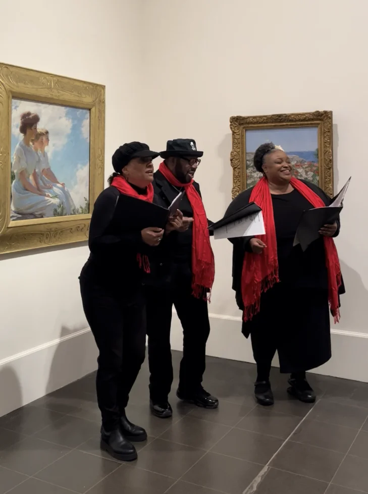 Three people in red scarves singing in the galleries