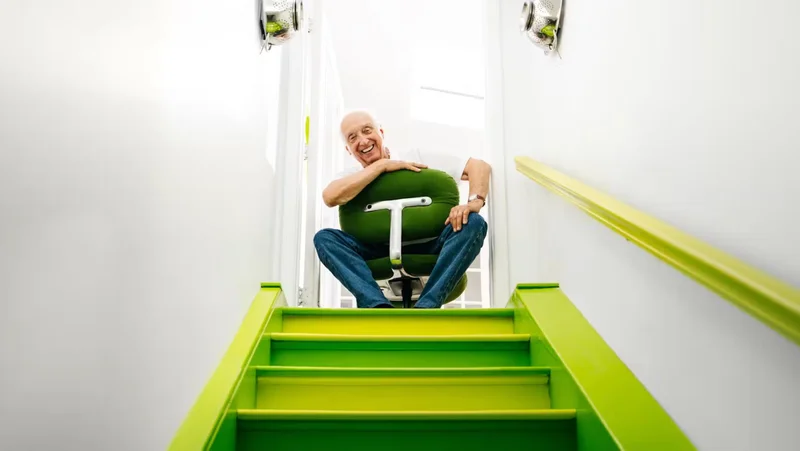 Bruce Hannah sits at the top of a lime green painted staircase with white walls in a kelly green upholstered Morrison Hannah chair with a white base.