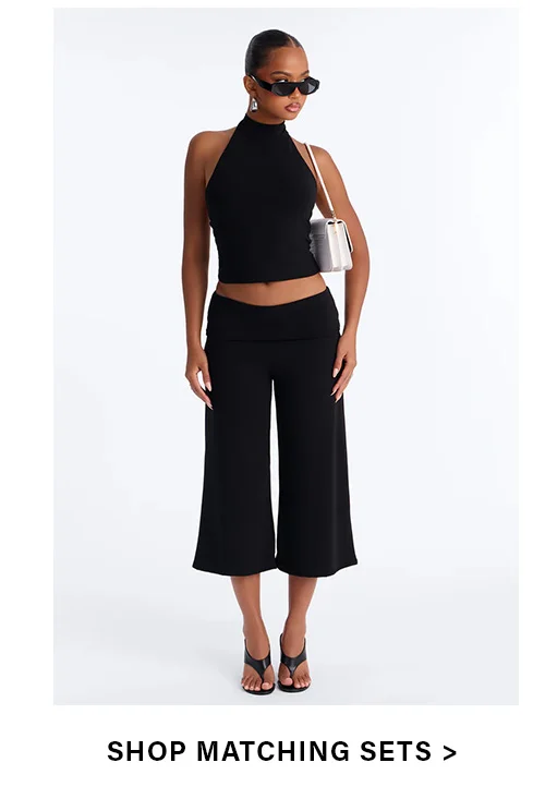 Chic black halter crop top & wide-leg cropped pants matching set for women. Stylish two-piece outfit with sunglasses & shoulder bag.