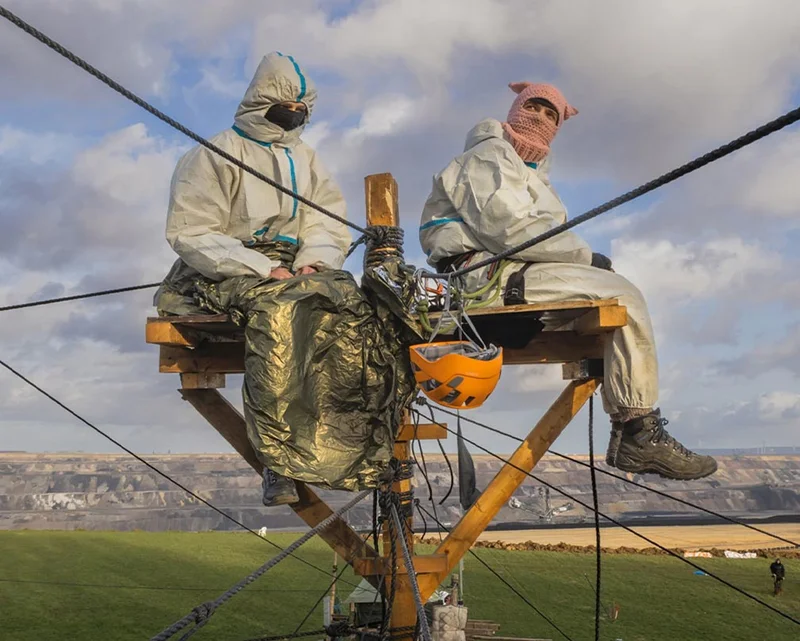 Two unidentifiable people sit high on a small platform with ropes connected to it.