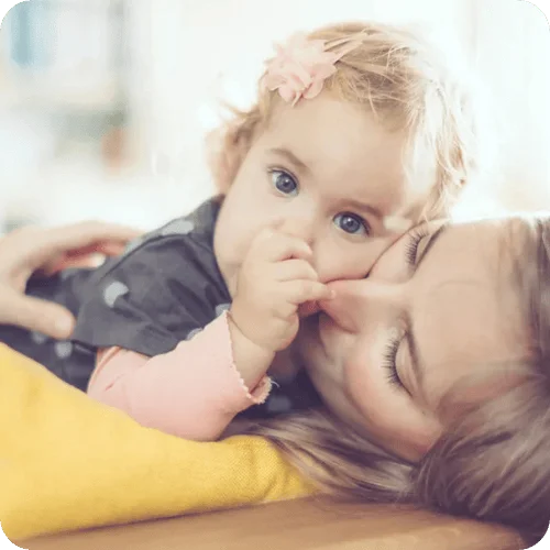 a toddler cuddling her mom while sucking her thumb