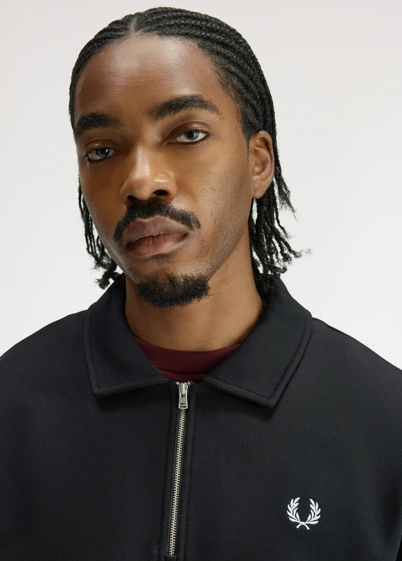 White male model with pale freckly skin and ginger short hair looks into the camera while wearing a collared half zip sweatshirt in ecru.